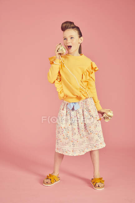 Брюнетка носит желтый топ и юбку с цветочным узором держа морской телефон скорлупы, на розовом фоне, игривый ребенок — стоковое фото