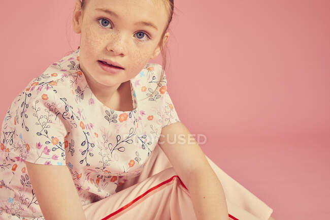 Porträt eines brünetten Mädchens, das ein florales Top auf rosa Hintergrund trägt und in die Kamera blickt — Stockfoto