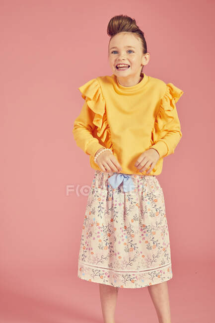 Portrait of brunette girl wearing yellow top and skirt with floral pattern on pink background, looking at camera with happy dace and smile — Stock Photo