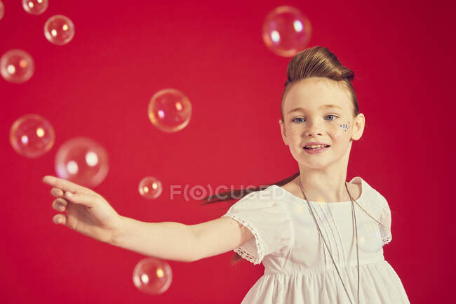 Portrait of brunette girl wearing romantic white dress on red background, surrounded by soap bubbles — Stock Photo