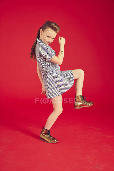 Cool linda chica en vestido posando sobre fondo rojo en estudio, baile de cuerpo entero y caminar - foto de stock