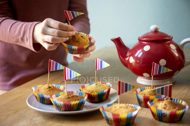 High angle view of red tea pot and decorated cupcakes on a kitchen table. — Stock Photo