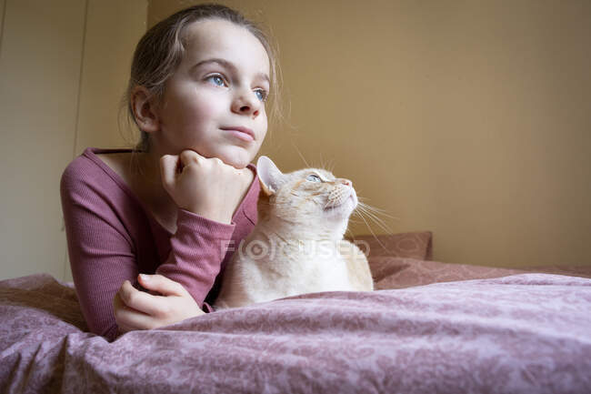 Porträt eines Mädchens und einer weißen Ingwerkatze, die auf dem Bett liegt. — Stockfoto
