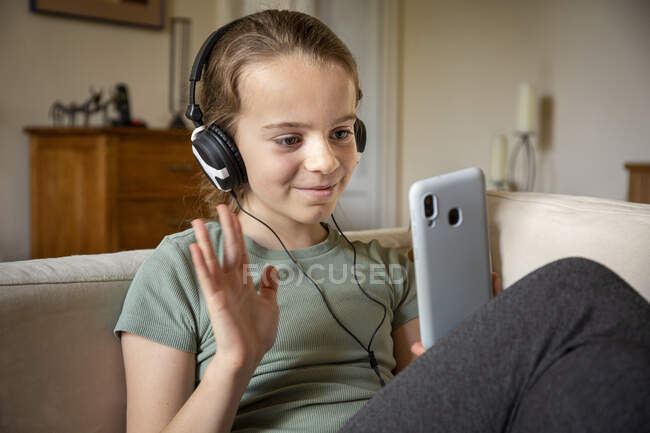 Mädchen mit Kopfhörern sitzt auf Sofa, hält Handy, chattet online. — Stockfoto
