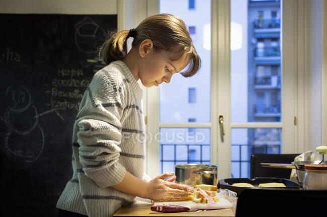 Chica de pie en una cocina, preparando comida. - foto de stock