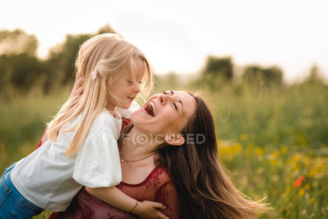 Jovem com cabelo loiro e mulher com longos cabelos castanhos abraçando em um prado, rindo. — Fotografia de Stock