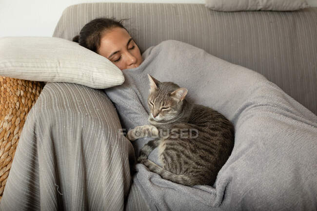 Woman and grey tabby cat sleeping on a sofa. — Stock Photo