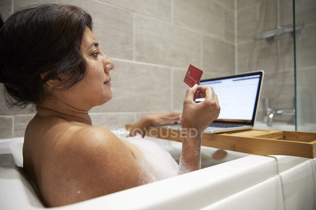 Mulher sentada na banheira, tendo banho de espuma e compras on-line em seu laptop durante a crise de Coronavirus. — Fotografia de Stock