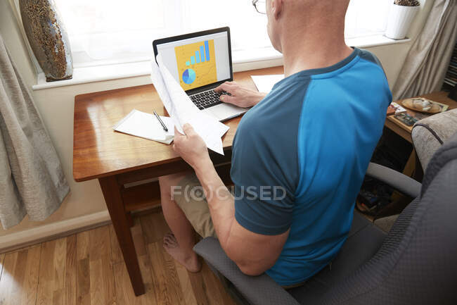 Человек, сидящий за маленьким столом, работающий дома во время коронавирусного кризиса. — стоковое фото