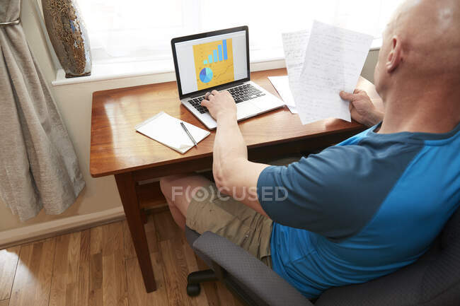 Homme assis en utilisant un ordinateur portable à un petit bureau, travaillant à la maison pendant la crise du coronavirus. — Photo de stock