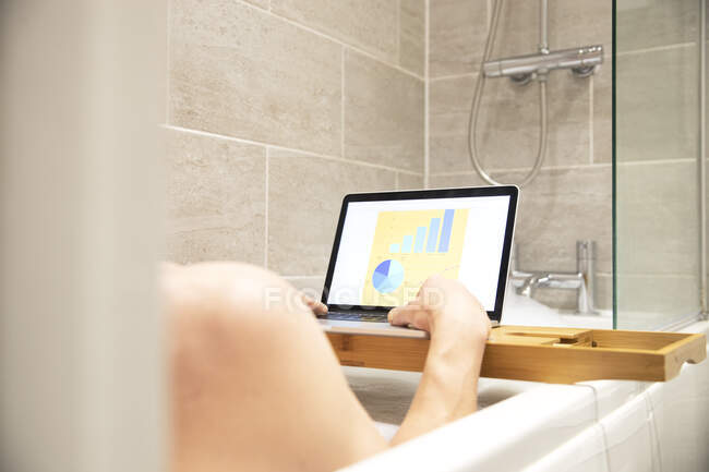 Mujer sentada en la bañera, teniendo baño de espuma y trabajando en el ordenador portátil durante la crisis de Coronavirus. - foto de stock