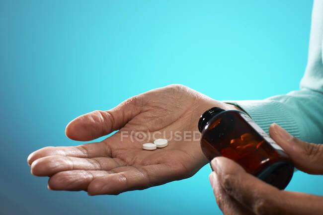 Primer plano de la persona que sostiene tabletas y frasco de píldora marrón, sobre fondo azul. - foto de stock