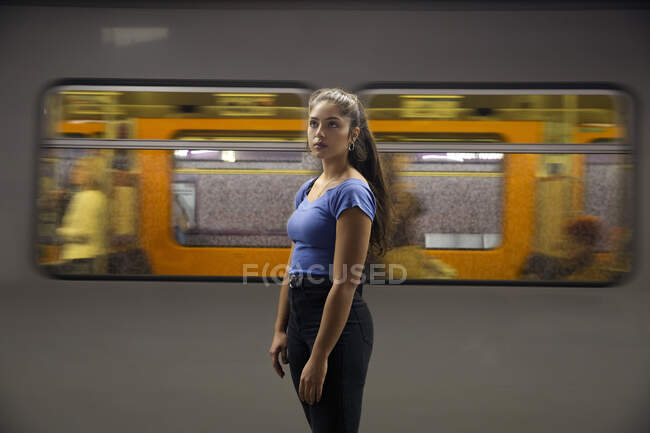 Mujer joven con el pelo castaño largo de pie delante del tren de cercanías en la plataforma de la estación de tren. - foto de stock