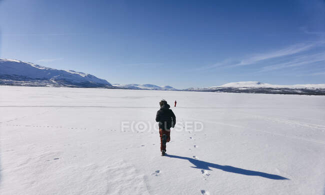 Rear view of two boys running across frozen lake in Vasterbottens Lan, Sweden. — Stock Photo