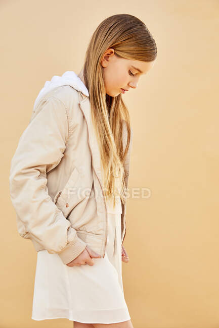 Porträt eines Mädchens mit langen blonden Haaren, das eine cremefarbene Kapuzenjacke trägt, auf blassgelbem Hintergrund. — Stockfoto