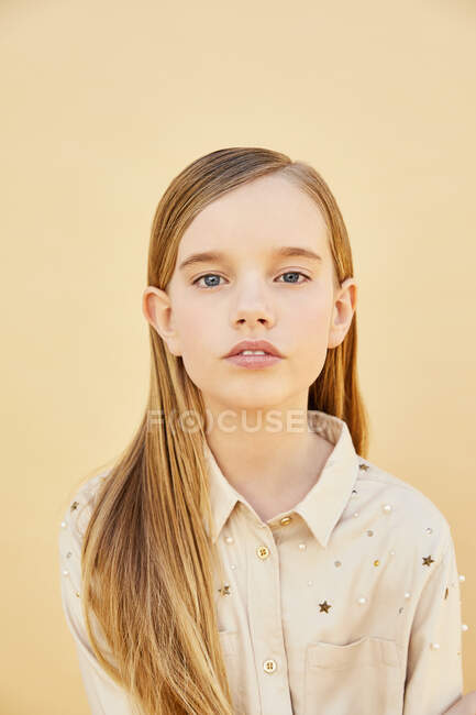 Retrato de menina com cabelos longos loiros vestindo camisa de cor creme, em fundo amarelo pálido. — Fotografia de Stock