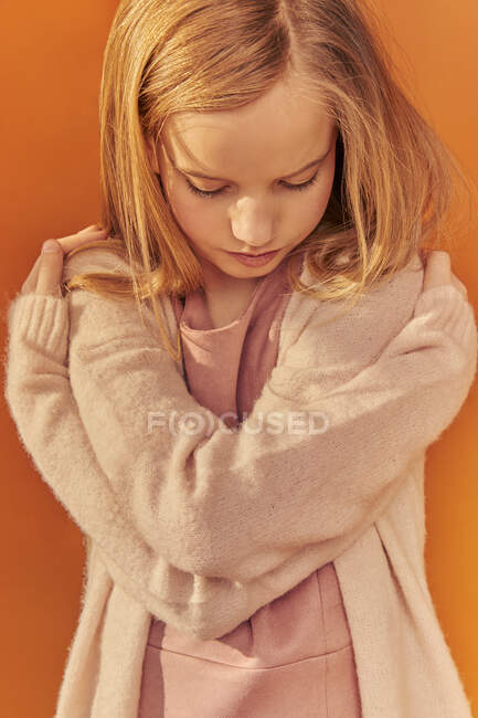 Retrato de niña con el pelo largo y rubio usando cárdigan de color crema, sobre fondo naranja. - foto de stock