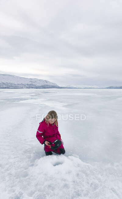 Girl looking at  ice-fishing hole on frozen lake in Vasterbottens Lan, Sweden. — Stock Photo
