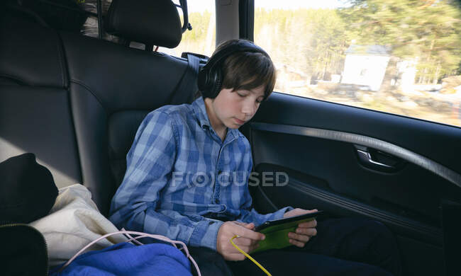 Niño sentado en un coche, con auriculares y la celebración de la tableta digital, Vasterbottens Lan, Suecia. - foto de stock