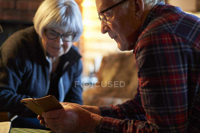 Älteres Paar sitzt an einem Tisch in einer Blockhütte und schaut auf sein Mobiltelefon, Vasterbottens Lan, Schweden. — Stockfoto