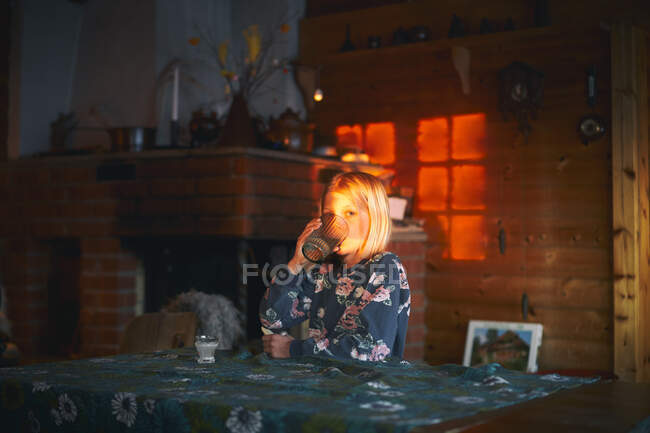 Menina sentada a uma mesa em uma cabine de madeira, beber um copo de água, Vasterbottens Lan, Suécia. — Fotografia de Stock
