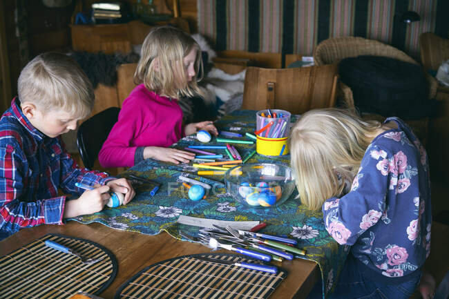 Ragazzo e due ragazze seduti a un tavolo in una baita, facendo artigianato, Vasterbottens Lan, Svezia. — Foto stock