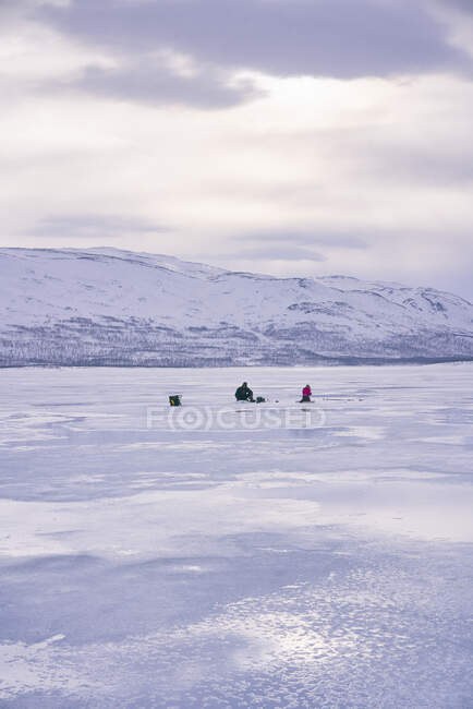 Distant view of two people ice-fishing on frozen lake in Vasterbottens Lan, Sweden. — Stock Photo