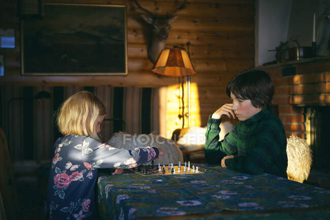 Garçon et fille assis à une table dans une cabane en bois rond, jouant aux échecs, Vasterbottens Lan, Suède. — Photo de stock