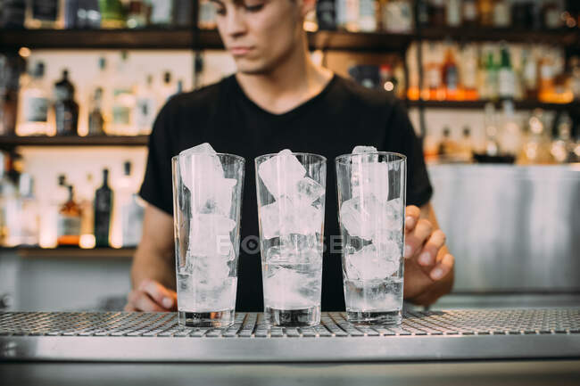 Jovem vestindo roupas pretas de pé atrás do balcão do bar, preparando bebidas. — Fotografia de Stock