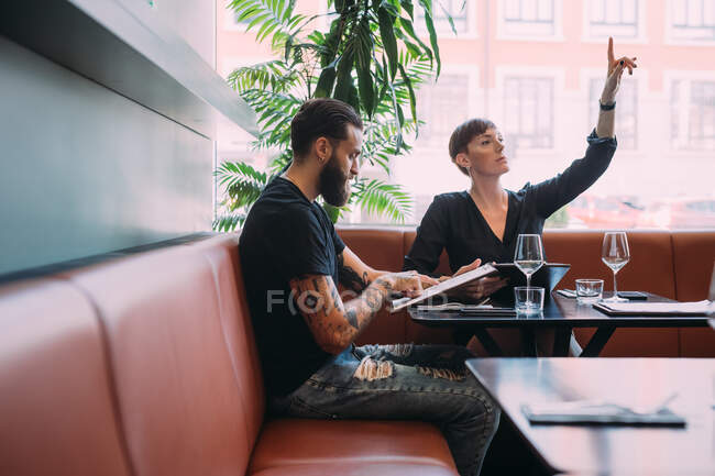 Young couple sitting at a table in a bar, woman beckoning for the bill. — Stock Photo