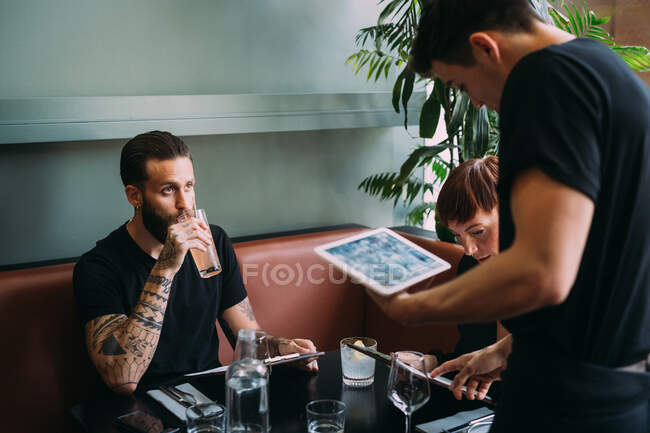 Waiter standing at a table in a bar, taking order using digital tablet. — Stock Photo