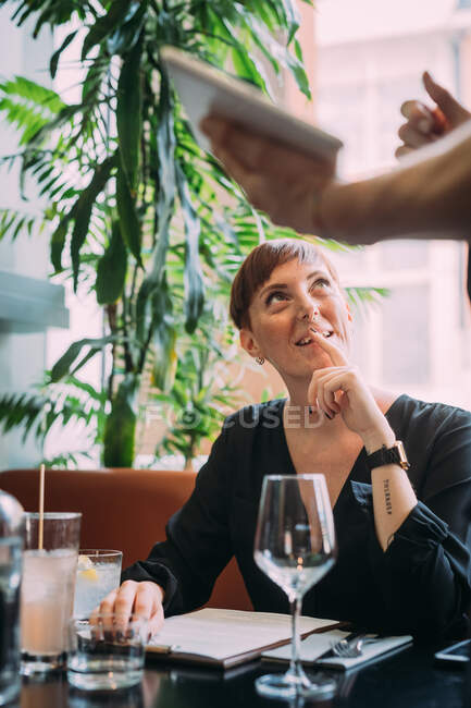 Молода жінка з коротким волоссям сидить у барі, посміхаючись офіціанту . — стокове фото