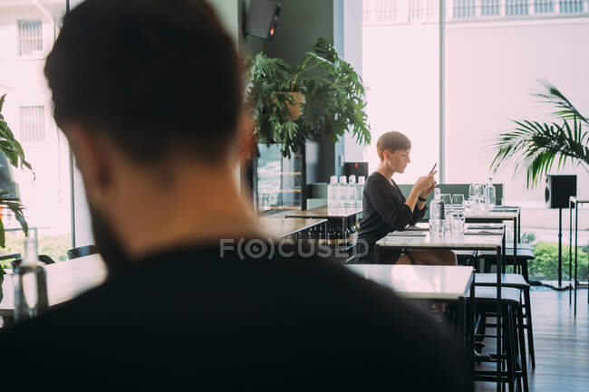 Вид ззаду чоловіка в барі, жінка сидить за столом на задньому плані . — стокове фото