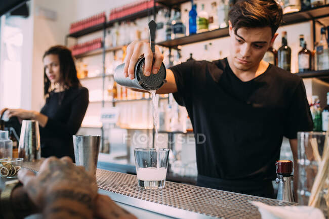 Young woman and man wearing black clothes standing behind bar counter, preparing drinks. — Stock Photo