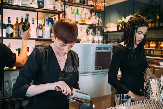 Deux jeunes femmes portant des vêtements noirs debout derrière le comptoir du bar, préparant des boissons. — Photo de stock