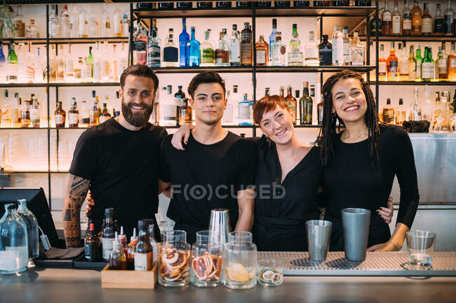 Portrait of two young women and men wearing black clothes, working in bar, smiling at camera. — Stock Photo