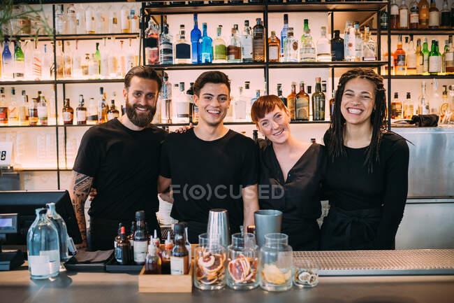Retrato de dos hombres y mujeres jóvenes vestidos de negro, trabajando en el bar, sonriendo a la cámara. - foto de stock