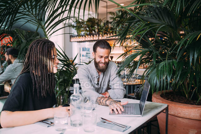 Young woman and bearded man sitting at a table in a bar, looking at laptop. — Stock Photo