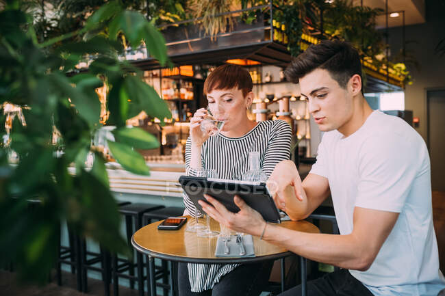Young woman and man sitting at a table in a bar, looking at digital tablet. — Stock Photo