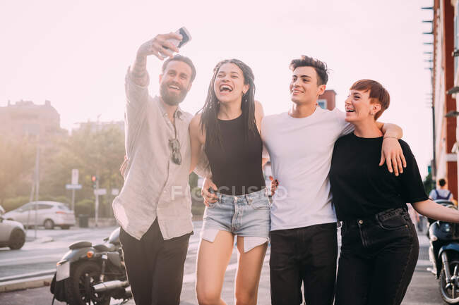 Zwei junge Frauen und Männer in Freizeitkleidung stehen auf einem Dach und machen ein Selfie mit dem Handy. — Stockfoto