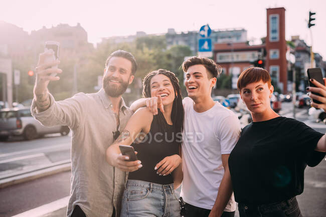 Dos mujeres jóvenes y hombres con ropa casual de pie en una azotea, tomando selfie con teléfono móvil. - foto de stock