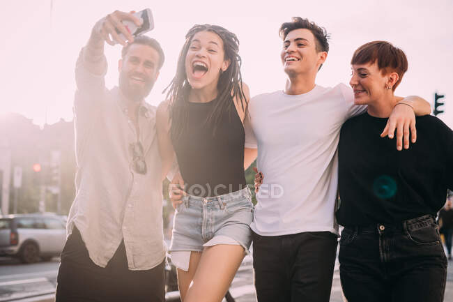 Dos mujeres jóvenes y hombres con ropa casual de pie en una azotea, tomando selfie con teléfono móvil. - foto de stock