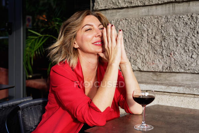 Портрет красивої ділової жінки в червоній куртці з світлим волоссям, червоне вино в склянці на столі, посміхаючись — стокове фото