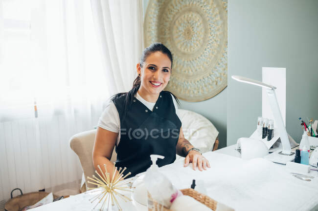 Beautician sitting at treatment table in beauty salon, smiling at camera. — Stock Photo