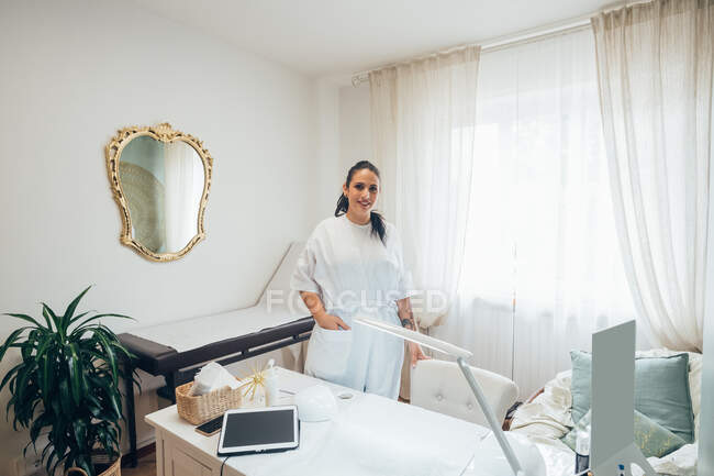 Esthéticienne debout au lit de traitement dans un salon de beauté, souriant à la caméra. — Photo de stock