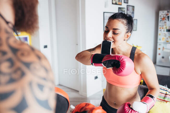 Bearded tattooed man with long brunette hair and woman with long brown hair standing indoors, practicing kickboxing. — Stock Photo