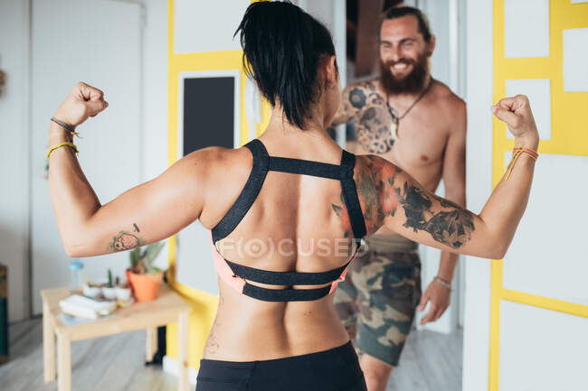 Одягнений татуюваннями чоловік з довгим волоссям брюнетки і жінка з довгим каштановим волоссям, що показує, як м'язи стоять у приміщенні.. — стокове фото