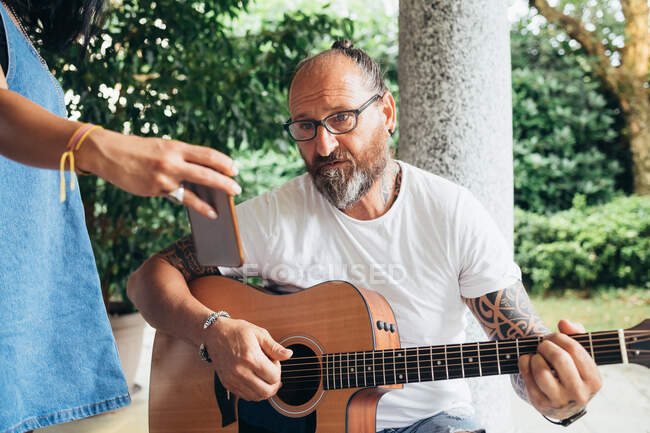 Бородатый татуированный мужчина с длинными волосами и в очках играет на гитаре. — стоковое фото