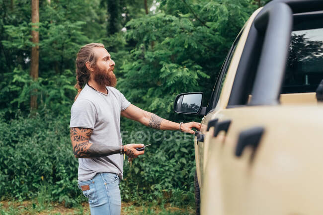 Bärtiger tätowierter Mann mit langen brünetten Haaren steigt in Pick-up-Truck. — Stockfoto