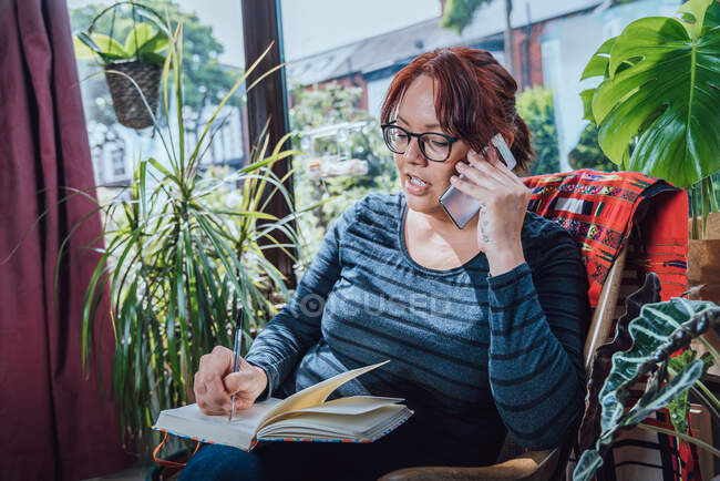 Woman working from home, on the phone in a conservatory during Corona virus crisis. — Stock Photo